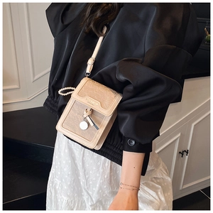 Detail of beige phone bag with pearl chain handle and metallic bow charm detail