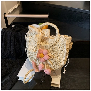 Détail du sac à main en paille tressée avec nœud en dentelle et charm fleur au crochet
