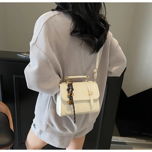 Detail of a cream structured crossbody bag with gold hardware and silk scarf handle