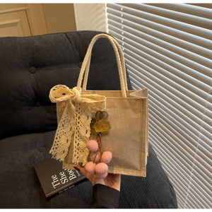 Close-up of beige woven tote bag with lace bow and pink fabric charm detail