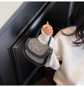 Detail of grey tweed saddle bag with black heart patterns and silver metal bow buckle