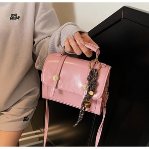 Close-up of a pink glossy square handbag with a gold buckle and woven charm detail