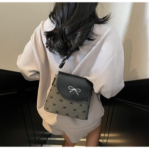 Detail shot of grey bow-patterned bucket bag with silver metal bow and black leather flap