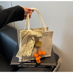 Detail of off-white woven tote bag featuring white lace bow and orange pumpkin charm