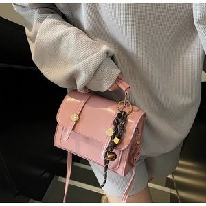 Detailed shot of pink patent leather crossbody bag with metallic buckles and striped charm