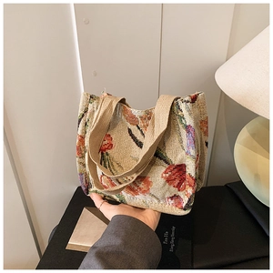 Primo piano di una borsa tote intrecciata con motivi floreali rossi e manici in tela