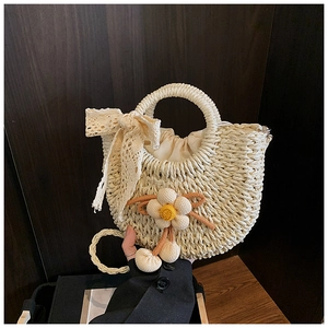 Détail du sac demi-lune en paille beige avec nœud en dentelle et fleur tricotée
