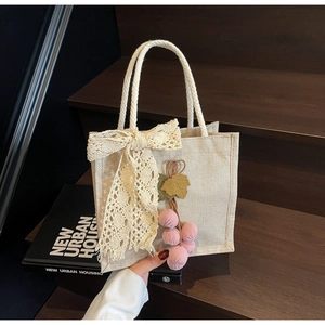 Close-up of beige woven handbag featuring lace bow and purple fabric grape charm details