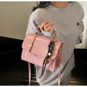 Detail view of pink crossbody bag with gold buttons and decorative woven charm pendant