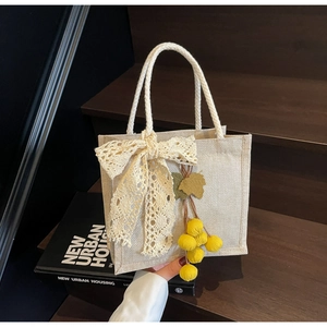 Detail of beige woven lunch bag featuring lace bow and bright yellow berry charms