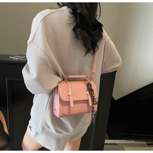 Pink square flap bag with metal buckles and floral scarf detail shown on shoulder