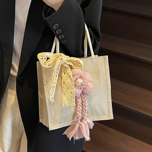 Borsa in lino beige con fiocco in pizzo giallo e ciondolo a fiore rosa su blazer nero