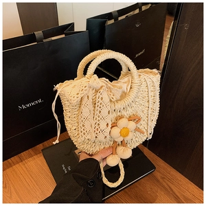 Détail d'un sac seau en paille avec nœud en dentelle, fleur en peluche et cordon serrage