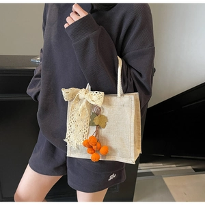Close-up of beige linen tote bag with lace bow and orange berry pendant detail