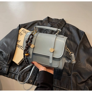 Close-up of light blue small square bag with golden hardware on a black leather jacket