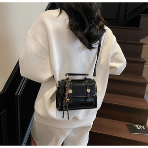 Detail of a black glossy crossbody bag with dual buckles and woven rope charm