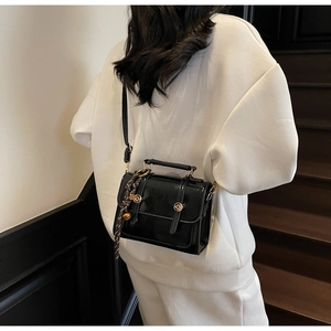 Detail of a vintage black patent leather crossbody bag with golden buckles and woven strap