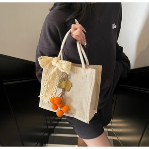 Detail of a beige woven lunch bag with lace bow and orange persimmon charms on stairs