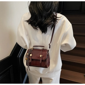 Detail of burgundy patent leather bag with gold buckle and striped silk scarf charm