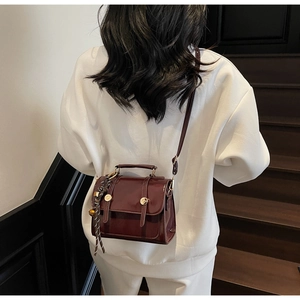 Detail of burgundy glossy crossbody bag with golden buckle and striped silk scarf