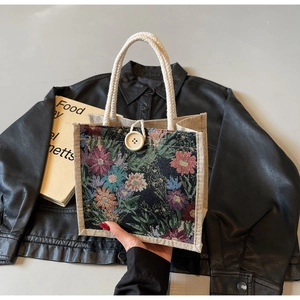 Detail of floral tapestry handbag with white button closure and woven rope handles
