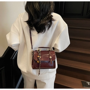 Detail of dark red glossy patent leather crossbody bag with a gold spherical charm pendant