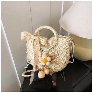 Détail du sac en paille fait main avec nœuds en dentelle et breloques fleurs au crochet