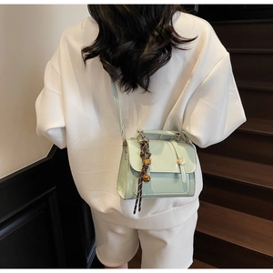 Detail of mint green crossbody bag with top handle and decorative plaid scarf charm