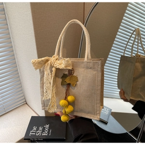 Close-up of beige jute tote bag with lace bow detail and decorative tassel pendant