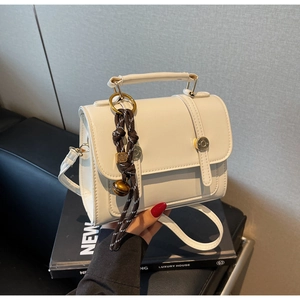 Detail of warm white PU leather crossbody bag with braided tassel and metal bell charm