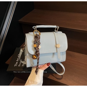 Detail view of light blue crossbody bag with vintage metal buckles and woven charm accessory
