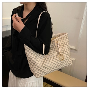 Detail of large tote bag with repetitive M pattern and gold metal pendant