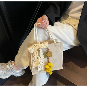Detail of beige jute tote bag with white lace bow and yellow fruit pendant charm
