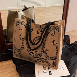 Close-up of natural jute tote bag featuring black scroll patterns and thick webbing handles