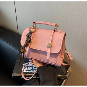 Detail view of pink crossbody bag with golden buckle and woven bell charm accessory