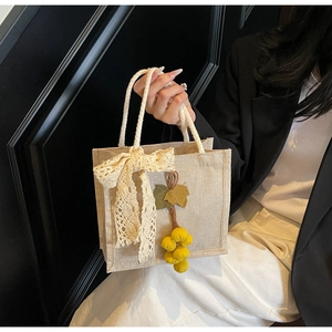 Detail of linen handbag featuring a lace bow, fruit charms, and woven handles