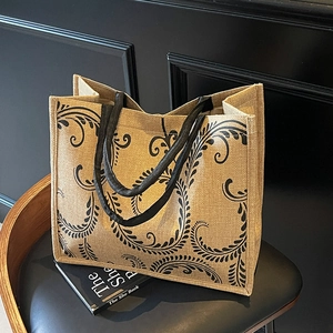 Detail of linen tote bag with black vine pattern on leather stool and dark background