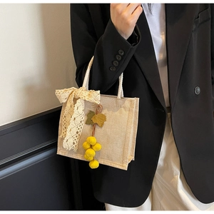 Close-up of beige linen handbag featuring lace bow decoration and yellow berry charm