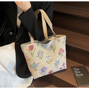 Detail of floral tapestry tote bag with canvas straps and a patch label on wood steps