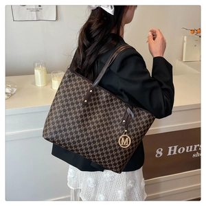 Detail of dark brown tote bag with letter pattern and metal M charm on a model