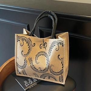 Detail of jute tote bag showing vintage floral print and black solid round handles