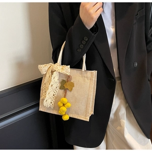 Detail of beige linen handbag featuring lace bow and decorative yellow fruit charm accessory