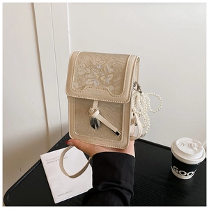 Detail view of beige floral jacquard phone bag with pearl chain and metal charm