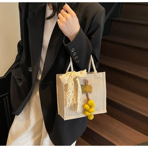 Detail of woven linen handbag with lace bow and yellow pom-pom charm on wooden stairs