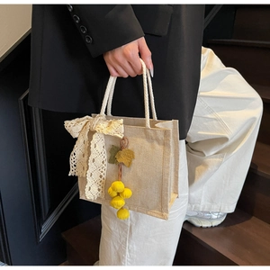 Detail of jute tote bag with lace bow decoration and yellow fruit pendant accessory