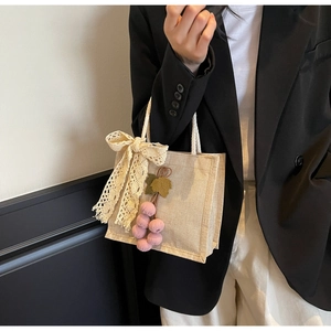 Close-up of beige woven tote bag with lace bow and plush grape charm detail