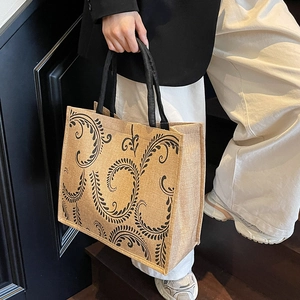 Detail of linen tote bag featuring black vintage floral patterns and woven handles