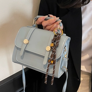 Elegant light blue PU leather crossbody bag with gold hardware and woven charm accessory