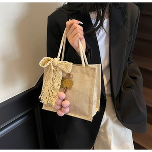 Detail of beige lace bow and pink grape charm on a woven canvas tote bag