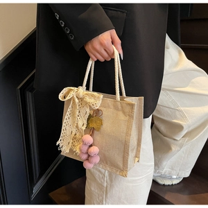Detail of beige linen handbag with lace bow, rope handles and pink plush keychain